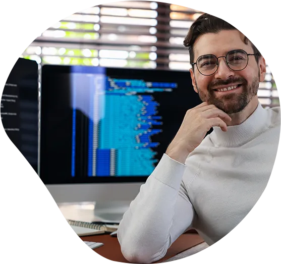 Ein freundlicher Entwickler lächelt vor seinem Arbeitsplatz in die Kamera