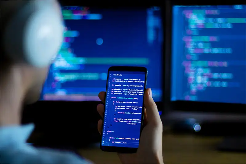 Ein Entwickler betrachtet Code auf Smartphone und Monitor