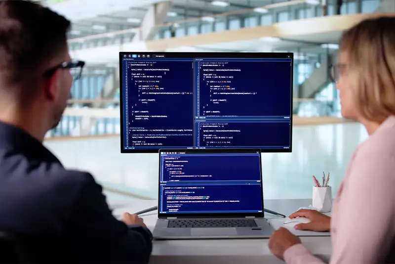 Zwei Developer betrachten Code auf übereinander gestapelten Bildschirmen