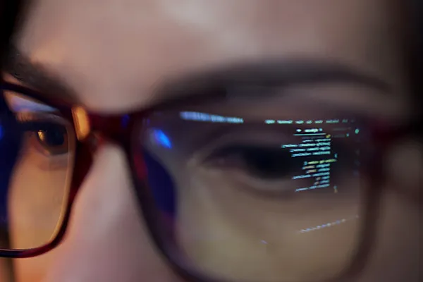 Computercode spiegelt sich auf der Brille einer jungen Programmiererin