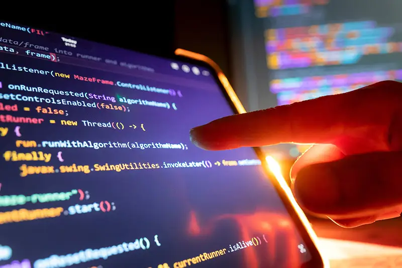 Eine Hand deutet auf einen Monitor mit Codezeilen