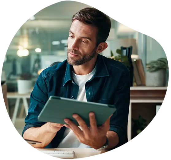 Ein Mann mit Tablet sitzt an seinem Arbeitsplatz und vergleicht Datensätze