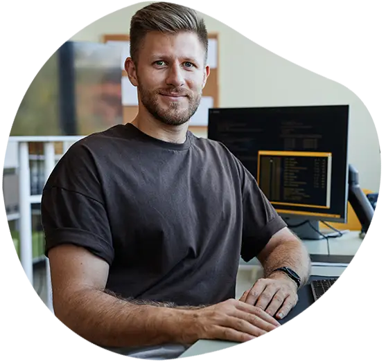 Ein zufriedener Geschäftsmann lächelt in die Kamera vor seinem Bildschirm mit Unternehmensdaten