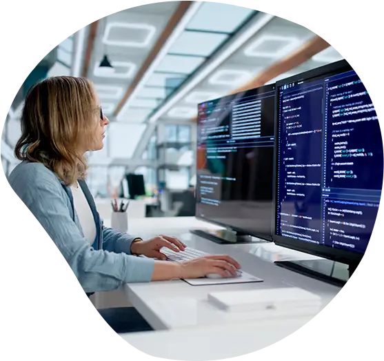 Eine Programmiererin arbeitet an ihren Bildschirmen mit Code