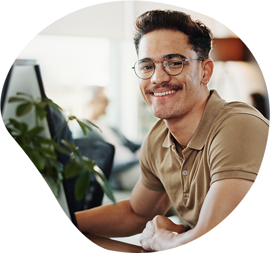 Ein Programmierer schaut lächelnd vom Arbeitsplatz in die Kamera