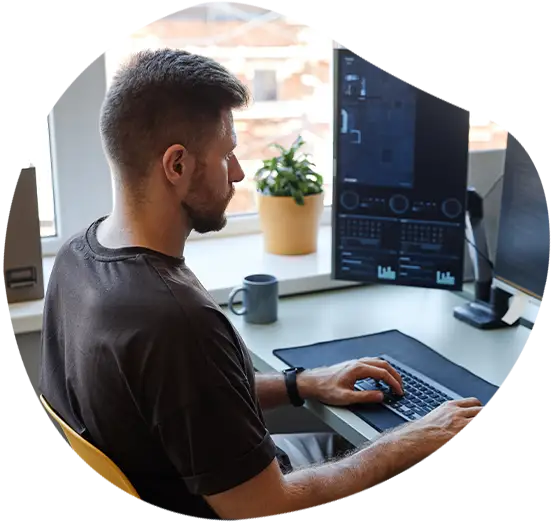 Porträt aus hoher Perspektive eines jungen Softwareentwicklers, der an seinem Arbeitsplatz mit mehreren Computerbildschirmen Code schreibt.