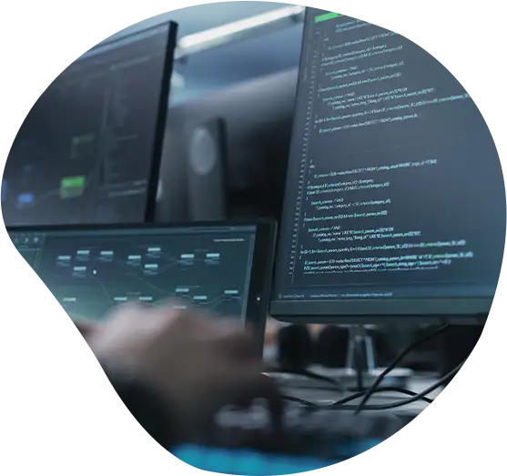 Person sitzt an einem Schreibtisch vor mehreren Monitoren.