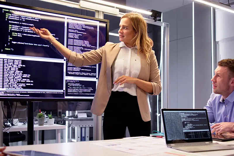 Eine Projektleiterin erklärt am großen Bildschirm