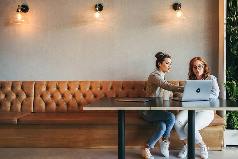 Zwei Kolleginnen sitzen mit einem Tablet in lockerer Atmosphäre