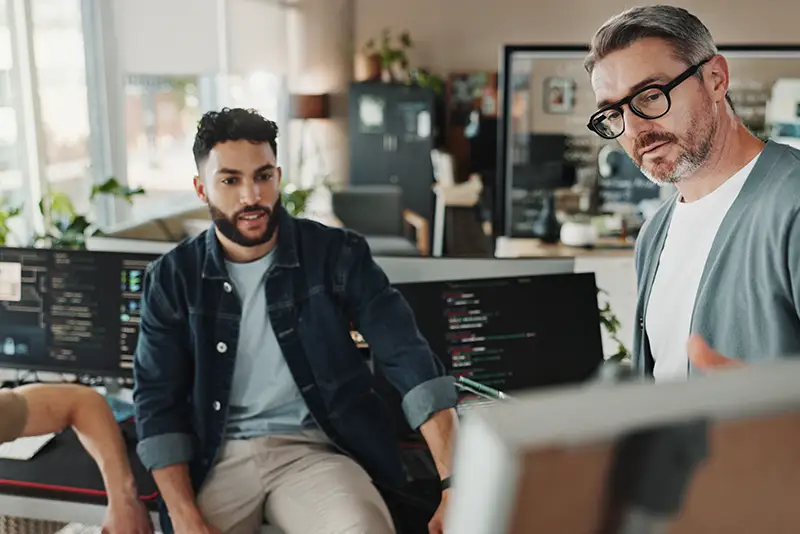 2 Mitarbeiter besprechen ihre Arbeit vor einem Bildschirm.