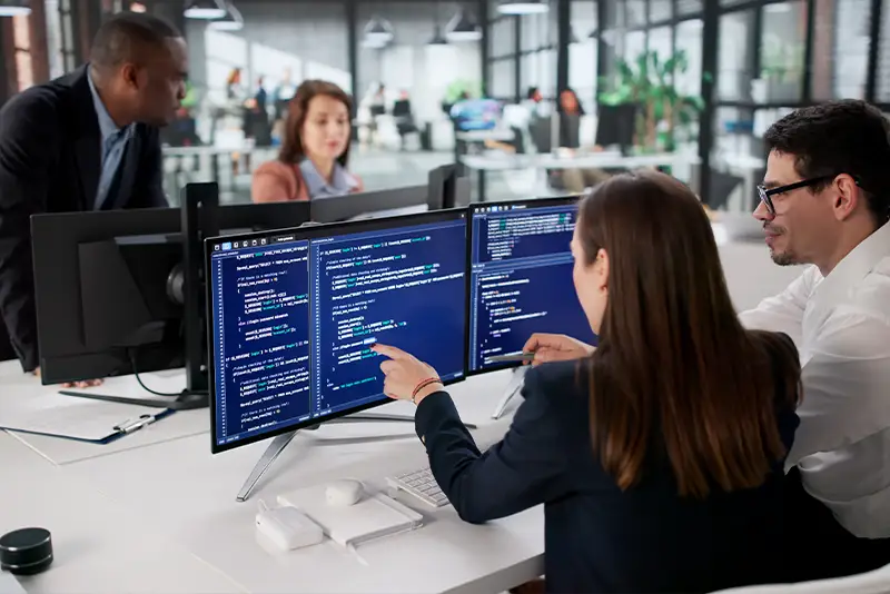 2 Mitarbeiter sitzen am Arbeitsplatz und schauen auf einen Bildschirm.