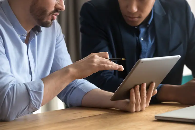 Geschäftsleute sitzen am Schreibtisch, sprechen miteinander und nutzen ein digitales Tablet, Nahaufnahme.