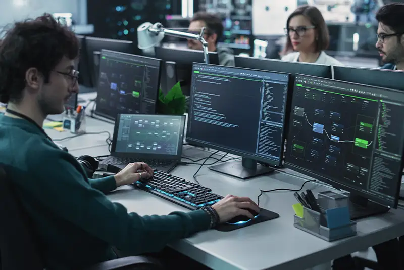 Ein diverses, multiethnisches Team von Softwareentwicklern arbeitet an Computern, programmiert fortschrittlichen Code und betreut online Projekte im Bereich künstliche Intelligenz.