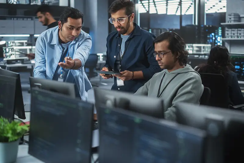 Ein Team aus drei Softwareentwicklern spricht, diskutiert und arbeitet gemeinsam an einem Projekt.